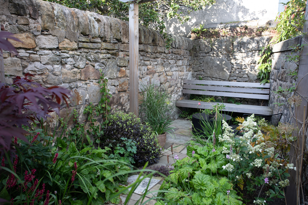 floating red cedar bench seen through the pergola and surrounded by a mix of herbaceous perennials and shrubs